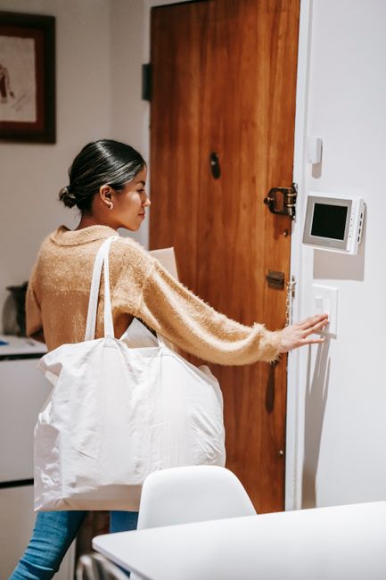 Ethnic dark haired female in casual outfit with shopping bag and boxes standing near door while couriering